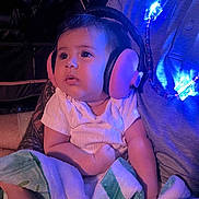 Raya is registered to the contest to win money with this photo: baby, headphones, blanket, tattoo, child, person, blue_light, infant, candid, indoor, striped_shirt, cute, seated, soft_texture, adult_arm, curious, wearing, cozy, closeup, comfort