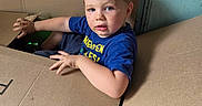 Tony is registered to the contest to win money with this photo: blond_hair, blue_eyes, blue_shirt, boy, candid, cardboard_box, child, curious, face, funny, garage, household, indoors, looking_at_camera, moving, plumbing, portrait, seated, storage, toddler