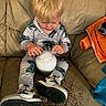 child, toddler, blond_hair, sitting, couch, portrait, indoor, home, clothing, striped_shirt, striped_pants, sneakers, orange_jacket, toy, white_object, playing, looking_down, hands, furniture, family_photo