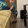 toddler, child, baby, portrait, standing, indoors, bedroom, bed, blanket, plaid_shirt, plaid_shorts, sandals, blond_hair, blue_eyes, looking_at_camera, furniture, wooden_door, heater, floor, home