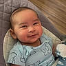 baby, smiling, blue_clothing, polar_bear_print, baby_chair, cushion, mittens, wooden_floor, indoors, infant, cute, happy, child, portrait, seated, young_child, cozy, comfortable, apparel, person