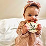 Josie is registered to the contest to win money with this photo: baby, infant, child, pink_dress, headband, sign, wooden_sign, months_old, six_months, cute, indoors, bed, white_bed, sitting, portrait, adorable, chubby_cheeks, bright_eyes, soft_light, warm_tones