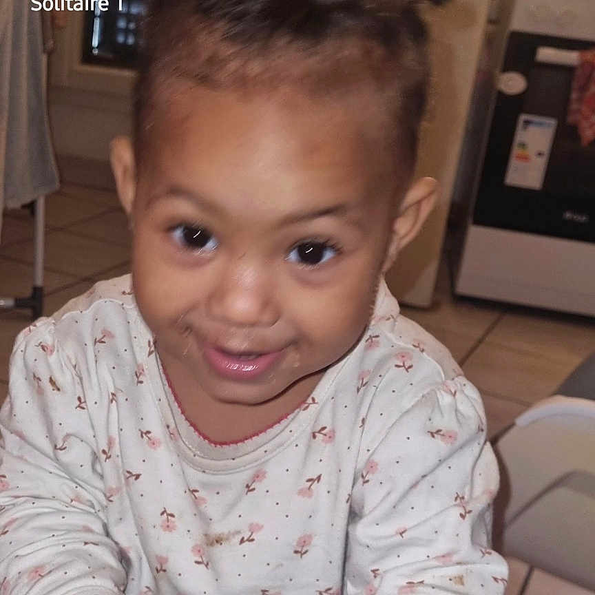 Joïa participe au concours pour gagner de l'argent avec cette photo : appliance, bread, casual_clothing, child, face, food, happy, home, indoor, kitchen, light_skin, person, playful, refrigerator, sitting, smiling, stove, tile_floor, toddler, young_child