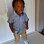 Jeremiah is registered to the contest to win money with this photo: toddler, child, boy, standing, white_shoes, patterned_shirt, khaki_pants, indoor, bench, curly_hair, expression, young, casual_clothing, portrait, person, small_child, fashion, cute, standing_pose, white_background