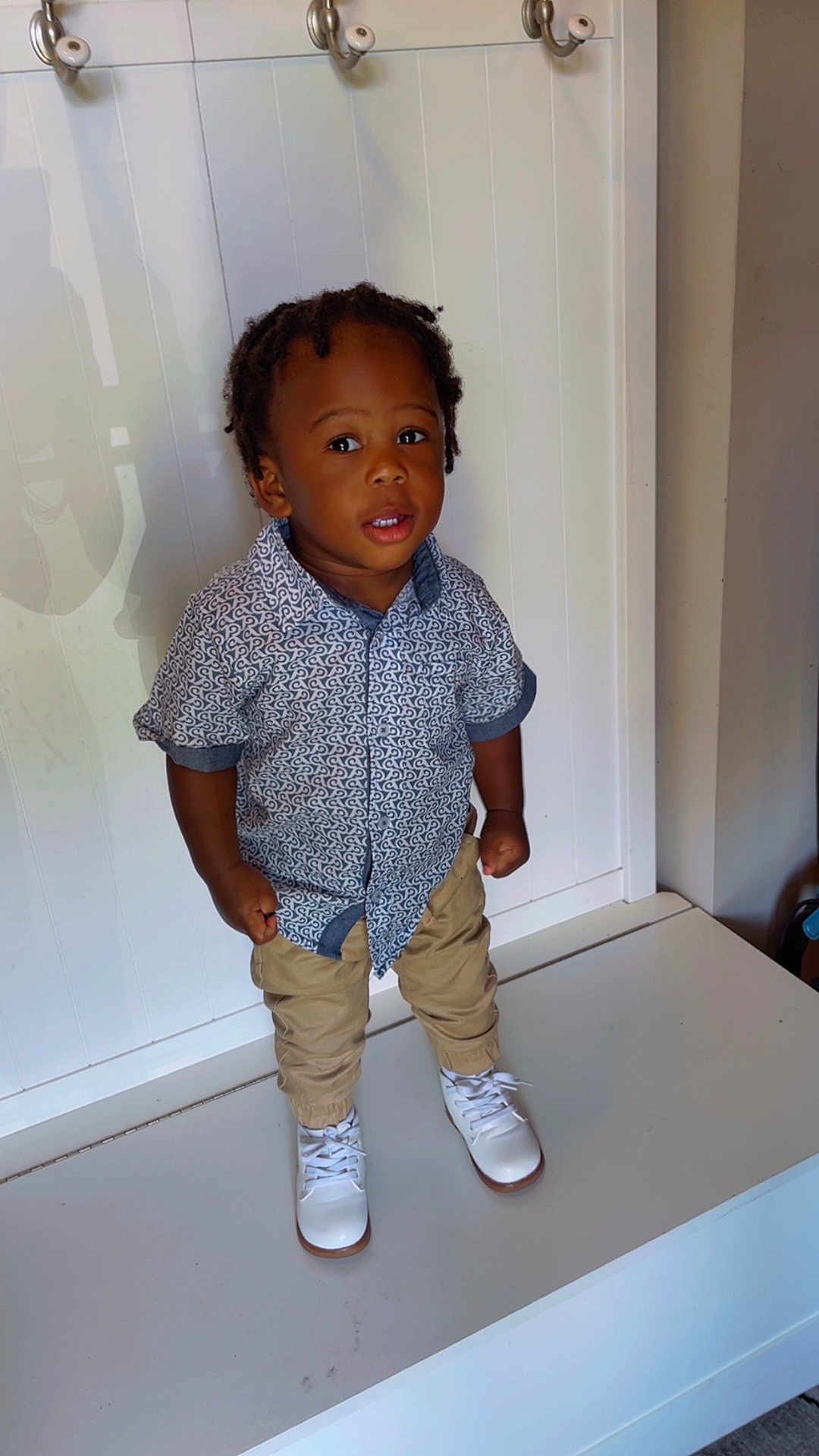 Jeremiah is registered to the contest to win money with this photo: toddler, child, boy, standing, white_shoes, patterned_shirt, khaki_pants, indoor, bench, curly_hair, expression, young, casual_clothing, portrait, person, small_child, fashion, cute, standing_pose, white_background