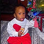 Jeremiah joined the competition — help win amazing prizes! toddler, child, christmas_tree, ornament, holiday, festive, red_pants, white_sweater, teddy_bear, carpet, stockings, fireplace, lights, decorations, indoors, cute, curious, sitting, celebration, home