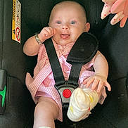 Rayna is registered to the contest to win money with this photo: baby, car_seat, infant, child, smiling, socks, pink_dress, seatbelt, toy, happy, cute, safety_harness, indoor, closeup, person, young_child, footwear, hand, face, playful