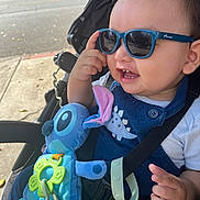 Dylan joined the competition — help win amazing prizes! toddler, child, sunglasses, smile, stroller, plush_toy, blue, outdoor, sunlight, toy, happy, baby, clothing, seatbelt, hand, face, cute, dinosaur, accessory, casual