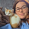 animal, blanket, cat, couch, cozy, cuddling, face, glasses, hoodie, indoor, kitten, natural_light, orange_white, pet, portrait, selfie, sitting, smiling, window, woman