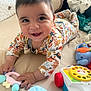 baby, smiling, toy, bed, pillow, onesie, hand, face, child, indoor, happy, cute, infant, playing, colorful, soft, lying_down, person, toddler, closeup