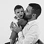 man, baby, child, father, parent, love, kiss, holding, overalls, shirt, chair, black_and_white, portrait, studio, expression, seated, affection, family, indoor, closeup