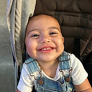 Mila joined the competition — help win amazing prizes! baby, child, smiling, face, denim_overalls, white_shirt, stroller, happy, cute, portrait, infant, person, clothing, seat, baby_toddler, skin, head, eyes, mouth, arm