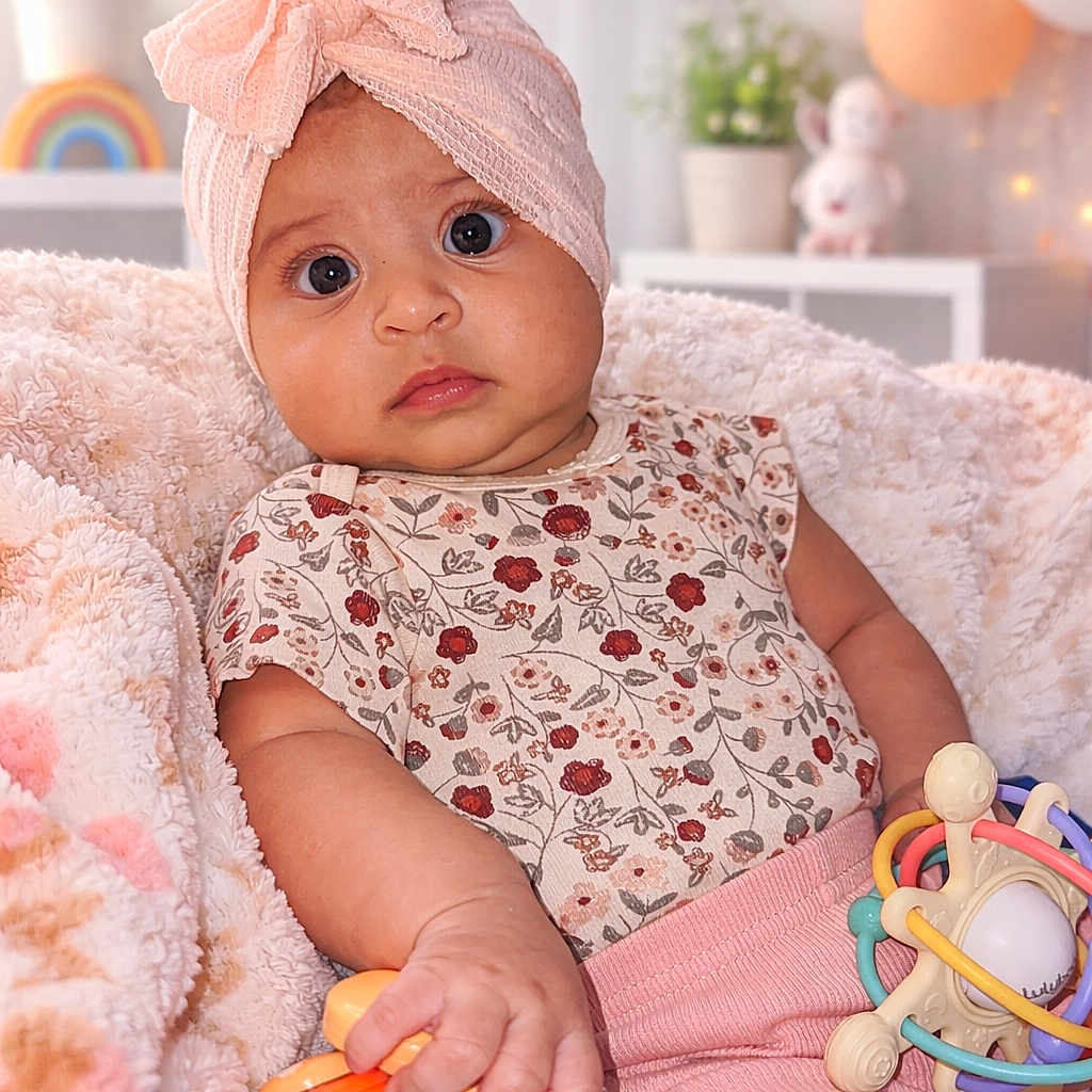 Eliana is registered to the contest to win money with this photo: baby, infant, child, headwrap, pink, blanket, toy, colorful, nursery, balloons, soft_lighting, face, expression, cute, indoor, decor, plant, smiling, clothing, sitting