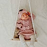 baby, sleeping, pink_outfit, knitted_clothing, bow, headband, pacifier, swing, beaded_rope, teddy_bear, soft_texture, white_background, infant, cute, cozy, footwear, child, peaceful, indoor, portrait