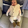 baby, infant, smile, couch, pillow, white_vest, boots, leggings, mittens, indoor, happy, child, furniture, cozy, portrait, seated, home_interior, cute, warm_clothing, relaxed