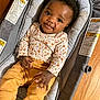 Ava joined the competition — help win amazing prizes! baby, infant, child, smiling, sitting, baby_seat, patterned_clothing, floral, mustard_pants, wooden_floor, indoors, cute, happy, young_child, portrait, person, clothing, seat, floor, relaxed