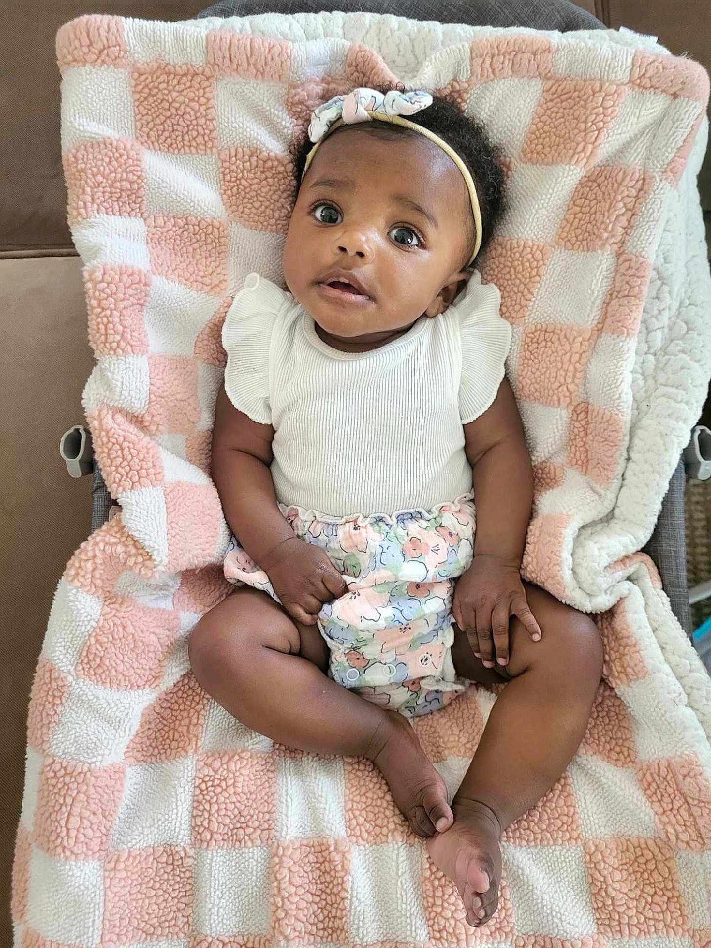 Ava joined the competition — help win amazing prizes! baby, infant, child, blanket, headband, clothing, patterned_clothing, pink, white, soft_texture, checkered_pattern, indoor, cute, portrait, lying_down, hand, foot, expression, person, young