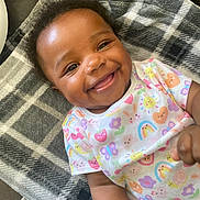 Ava joined the competition — help win amazing prizes! baby, smiling, infant, child, blanket, plaid, clothing, pattern, colorful, cute, happy, face, portrait, laying, indoors, person, skin, toddler, short_sleeve, expression