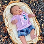 baby, basket, plaid_shorts, pink_shirt, sunglasses_patch, autumn_leaves, mulch, outdoor, infant, smiling, clothing, fabric, woven, foot, hand, face, nature, seasonal, relaxed, portrait