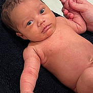 Elijah is registered to the contest to win money with this photo: baby, infant, skin, hand, finger, adult_hand, towel, lying_down, closeup, expression, moisture, newborn, human, portrait, curious, young_child, resting, soft_skin, baby_arm, baby_face