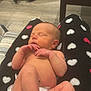 newborn, baby, sleeping, diaper, blanket, heart_pattern, infant, person, hand, foot, table, baby_bottle_nipple, snack, indoor, flooring, legs, skin, relaxing, comfort, cozy