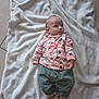 baby, blanket, floor, tile, clothing, pants, socks, person, infant, cute, indoor, soft, fabric, pattern, floral, bow, small, lying_down, footwear, young_child