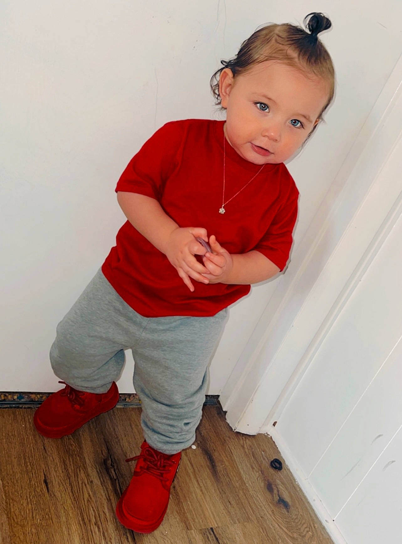 Kian is registered to the contest to win money with this photo: arm, baby_toddler_clothing, dress, face, floor, flooring, hair, hardwood, human_body, human_leg, knee, laminate_flooring, person, shoe, sleeve, sportswear, t_shirt, thigh, toddler, wood