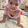 baby, crawling, smiling, tongue_out, pink_dress, headwrap, play_mat, toys, indoor, child, cute, happy, infant, floor, person, home, colorful, pattern, young_child, toddler