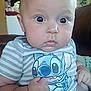 baby, infant, child, person, face, eyes, hand, fist, clothing, striped_shirt, cartoon_character, indoor, wooden_wall, couch, furniture, curious_expression, closeup, portrait, cute, homedecor