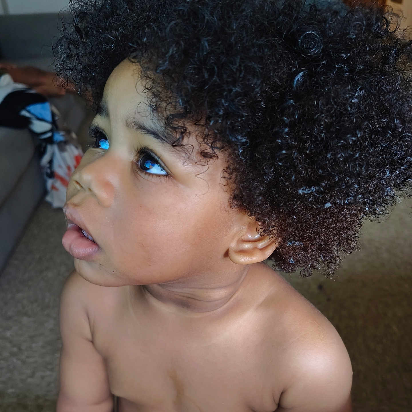 Kaleb is registered to the contest to win money with this photo: toddler, child, curly_hair, indoor, portrait, baby, skin, expression, eyes, face, hair, person, young_child, couch, living_room, curiosity, close_up, natural_light, cute, bare_chest
