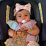 baby, child, infant, pacifier, headband, car_seat, tattoo, hand, pink_clothing, patterned_pants, blanket, indoor, cute, holding_hand, person, seated, closeup, soft_lighting, comfortable, adorable