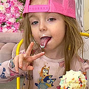 Jocyne is registered to the contest to win money with this photo: child, girl, ice_cream, cone, sprinkles, pink_cap, long_hair, peace_sign, tongue_out, floral_background, yellow_chair, pink_dress, cartoon_print, happy, indoor, sweet, colorful, playful, messy_face, fun