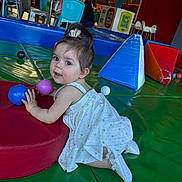 Mélya participe au concours pour gagner de l'argent avec cette photo : toddler, child, indoor, play_area, colorful, ball, red_cushion, blue_cushion, white_dress, playground, person, floor_mat, toy, young_child, curly_hair, play, happy, cute, baby_shoes, activity