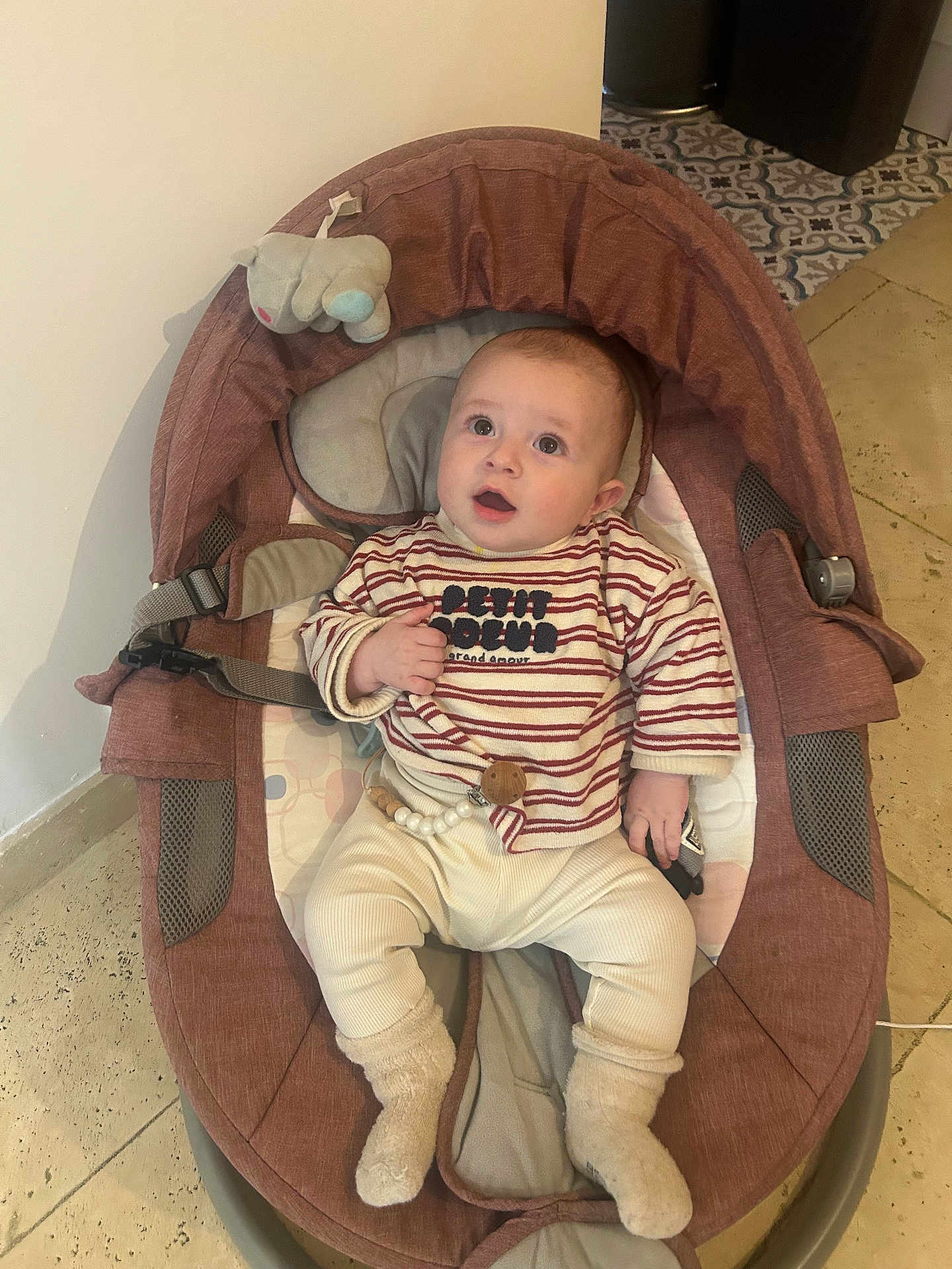 Manny participe au concours pour gagner de l'argent avec cette photo : baby, infant, child, rocker, baby_rocker, striped_shirt, socks, soft_toy, elephant_toy, flooring, tile_floor, curious, seated, indoor, clothing, cute, baby_clothes, expression, face, person
