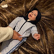 Manny participe au concours pour gagner de l'argent avec cette photo : baby, child, blanket, brown, clothing, hood, hand, happy, infant, laying_down, person, plush, reaching, smiling, soft, toddler, wearing, young, cute, indoor