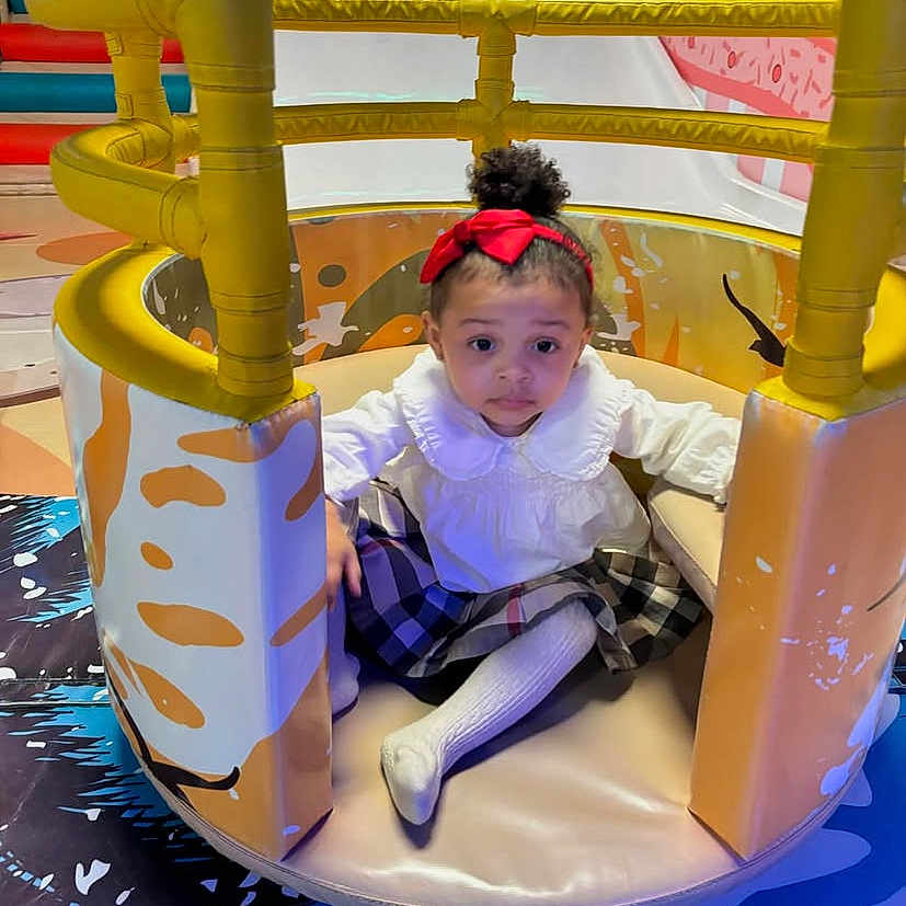 Crisamiah joined the competition — help win amazing prizes! child, colorful, curly_hair, cute, floor_mat, fun, girl, indoor_play_area, looking_at_camera, padded, plaid_skirt, play_structure, playground, portrait, red_bow, sitting, soft_expression, toddler, white_blouse, young_child