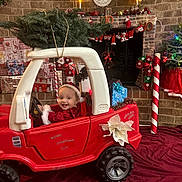 Nevaeh joined the competition — help win amazing prizes! toddler, child, toy_car, christmas_tree, holiday_decorations, candy_canes, wrapped_presents, fireplace, brick_wall, festive_clothing, santa_hat, smiling_child, indoor, red_car, christmas_lights, poinsettia, garland, holiday_spirit, cheerful, seasonal