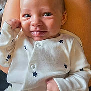 Charlie joined the competition — help win amazing prizes! baby, infant, onesie, white_clothing, stars_pattern, tongue_out, smiling, face, hands, skin, person, cute, young_child, sitting, lap, happy, playful, indoor, closeup, portrait