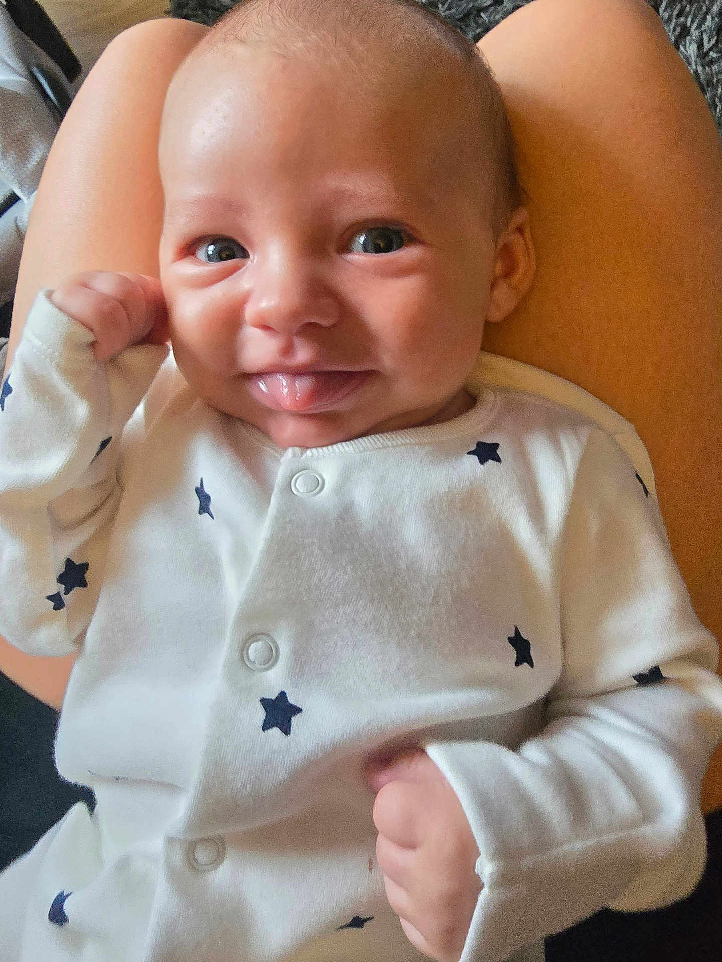 Charlie joined the competition — help win amazing prizes! baby, infant, onesie, white_clothing, stars_pattern, tongue_out, smiling, face, hands, skin, person, cute, young_child, sitting, lap, happy, playful, indoor, closeup, portrait