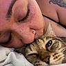 affection, bed, bedding, cat, close_up, cozy, cuddling, face, fur, green_eyes, indoors, nose, person, pet, piercing, portrait, sleepy, tabby_cat, tattoo, whiskers