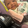 baby, smile, car_seat, bib, infant, closeup, face, happy, child, cute, soft_toy, fabric, warning_label, seatbelt, indoors, person, skin, head, clothing, expression