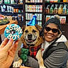dog, person, party_hat, birthday, treat, hand, sunglasses, winter_hat, smile, pet_store, shelf, food_packages, counter, celebration, festive, happy, indoor, clothing, paw, toy