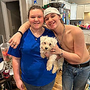Max is registered to the contest to win money with this photo: bracelet, cabinet, cap, casual_clothing, dog, friendship, happy, home, indoor, jeans, kitchen, necklace, person, pet, refrigerator, shirtless, smiling, table, white_dog, wood_floor