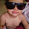 baby, child, curly_hair, sunglasses, portrait, indoors, seated, close_up, face, lips, skin, infant, fashion, funny, looking_at_camera, blanket, red_fabric, purple_clothing, home, photography