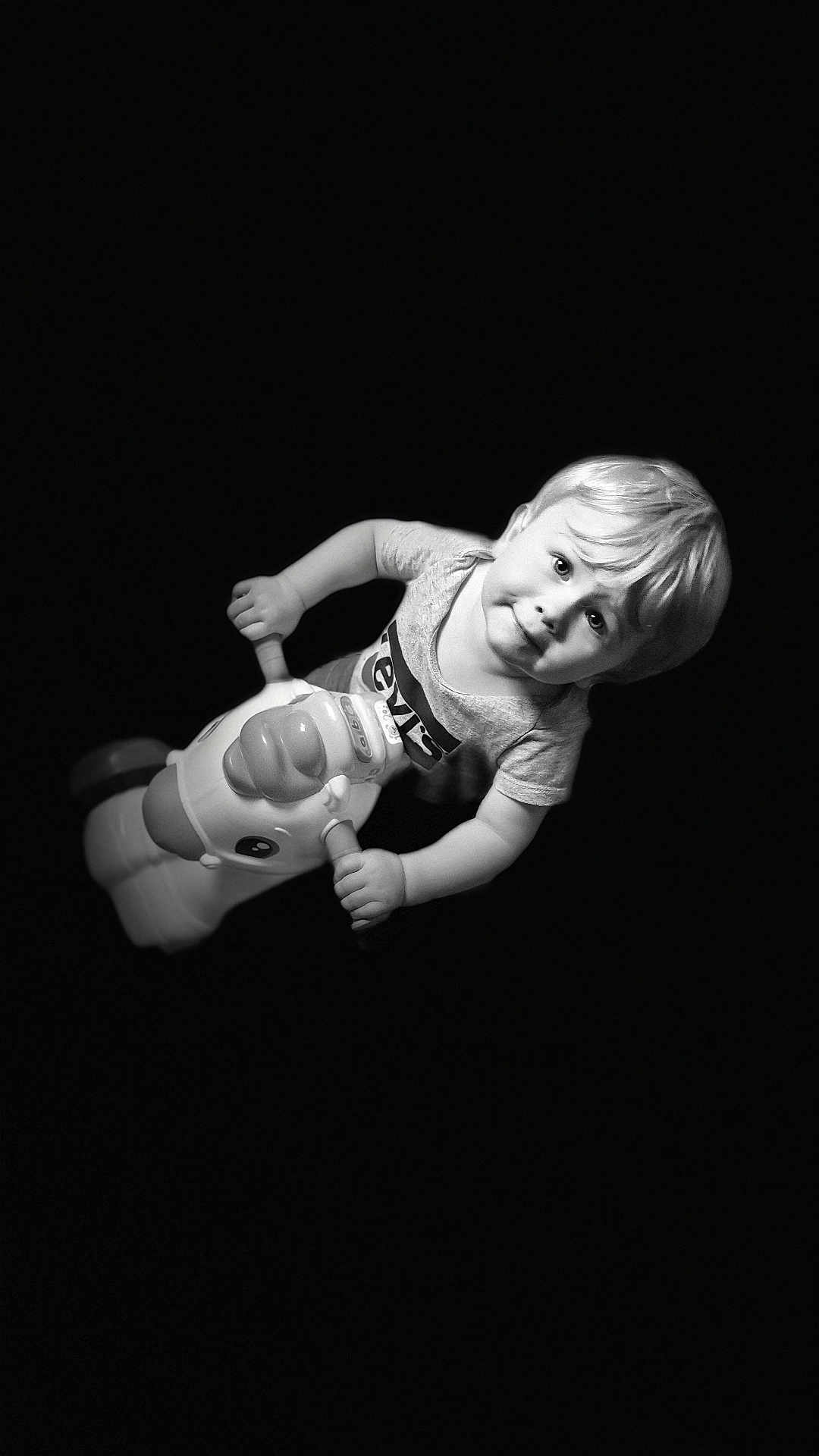 Dayvenn participe au concours pour gagner de l'argent avec cette photo : toddler, child, toy, unicorn, riding, playful, curious, black_background, monochrome, portrait, young_child, fun, cute, smiling, blond_hair, short_sleeves, indoor, isolated, floating, happy