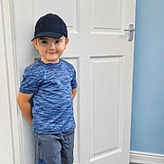 Corey joined the competition — help win amazing prizes! blue_shirt, boy, cap, casual_clothing, child, feet, floor, happy, indoor, light, person, portrait, room, shorts, smile, sneakers, socks, standing, wall, white_door