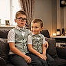 children, brothers, portrait, sitting, sofa, living_room, formalwear, vest, bow_tie, glasses, smiling, indoors, family, siblings, young, boy, furniture, home, warm_lighting, photography