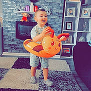 Corey joined the competition — help win amazing prizes! toddler, child, indoor, carpet, inflatable_toy, orange, toy, happy, smiling, footwear, home, furniture, photoframe, television, fireplace, brick_wall, shelf, plant, couch, casual_clothing