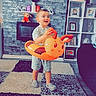 toddler, child, indoor, carpet, inflatable_toy, orange, toy, happy, smiling, footwear, home, furniture, photoframe, television, fireplace, brick_wall, shelf, plant, couch, casual_clothing