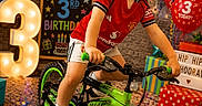 Corey joined the competition — help win amazing prizes! balloons, bike, birthday, celebration, child, colorful, confetti, decorations, festive, floor, happy, indoor, lighting, number_3, party, presents, red_shirt, smiling, training_wheels, young_boy